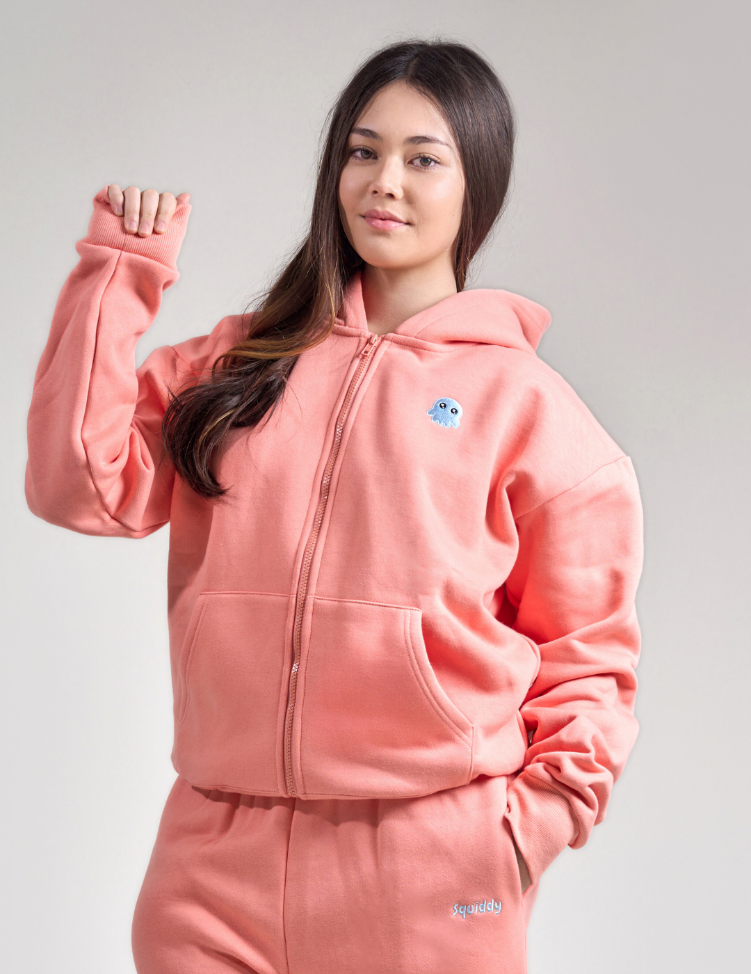 Person wearing a peach colour hoodie with a logo on a gray background